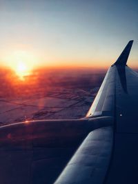 Airplane wing against sky during sunset