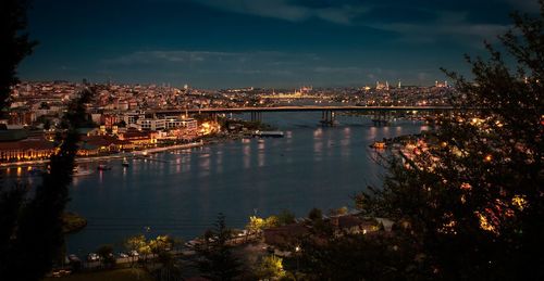 Illuminated buildings by river against sky at night