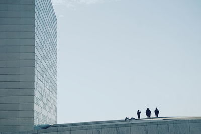 Low angle view of people walking on modern building against sky