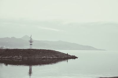 Lighthouse at shore against sky during foggy weather