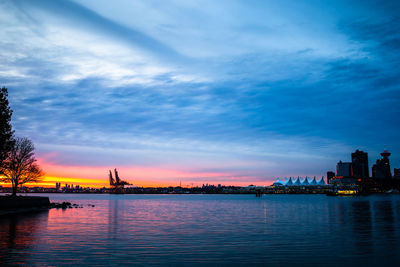 Scenic view of river by buildings against sky during sunset