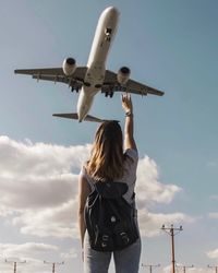 Rear view of woman waving at airplane flying in sky