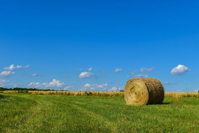 Hay bales on field against blue sky