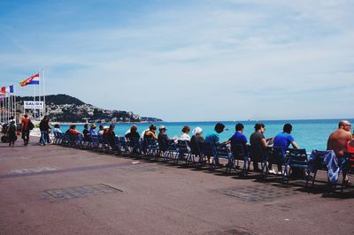Rear view of people sitting on chairs at promenade