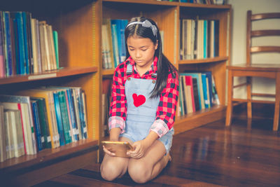 Girl using digital tablet while kneeling in library