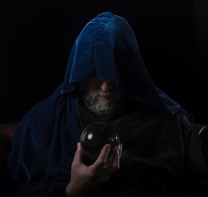 Man with hooded shirt holding crystal ball against black background