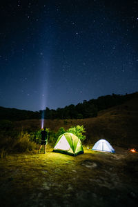 Tent on field against sky at night with photographer man hold flashlight to sky