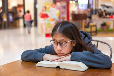 Close-up of bored girl leaning on book at library