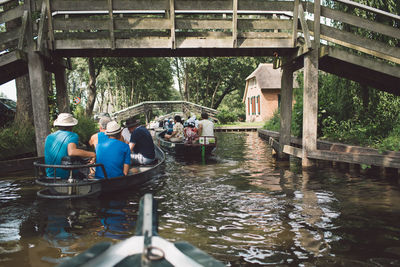 Rear view of people on boats sailing in river below bridge