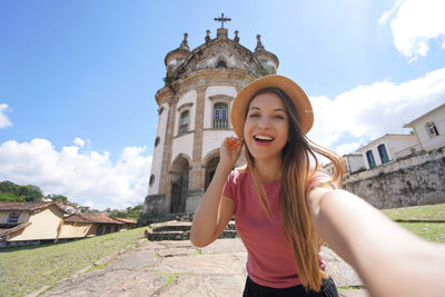 Woman taking self portrait with the church of our lady of the rosary in ouro preto, brazil.