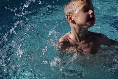 Close-up of shirtless boy swimming in turquoise pool