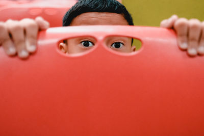 Cropped portrait of boy looking through holes in red chair