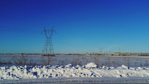 Electricity pylon on snow covered field against clear sky