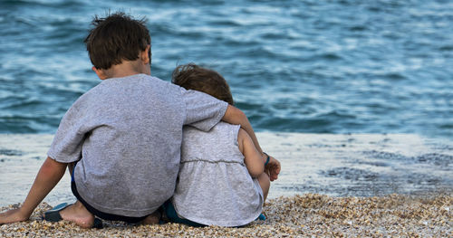 Rear view of siblings sitting at beach