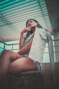 Portrait of beautiful young woman wearing eyeglasses while sitting on rooftop