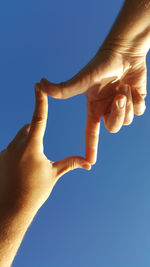 Close-up of hands against blue sky