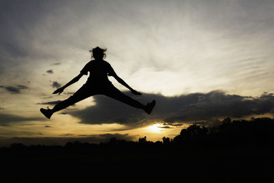 Silhouette person paragliding on field against sky during sunset