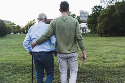 Back view of young man assisting his grandfather walking