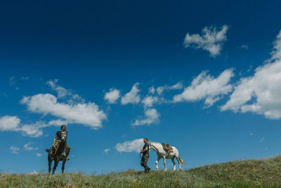 Woman riding horse with friend on field against sky