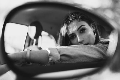 Young woman reflecting on side-view mirror of car