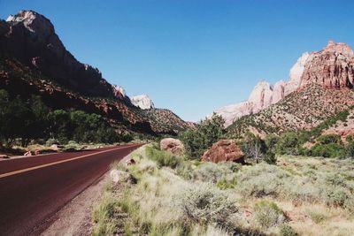 Road leading towards mountains against clear blue sky
