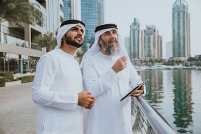 Male coworkers discussing over digital tablet while standing in city