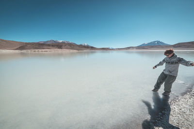 Man standing on lake against clear blue sky