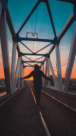 Rear view of man standing on bridge against sky during sunset