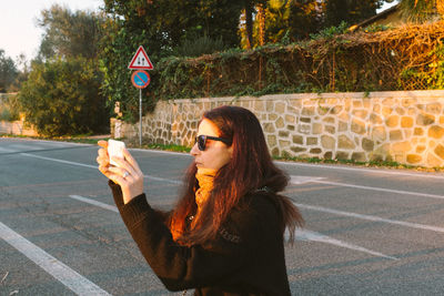 Woman photographing on street during sunset