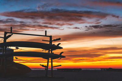 Surf boards silhouetted against vibrant yellow and orange sky with clouds after sunset