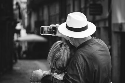 Rear view of man wearing hat and a woman standing outdoors