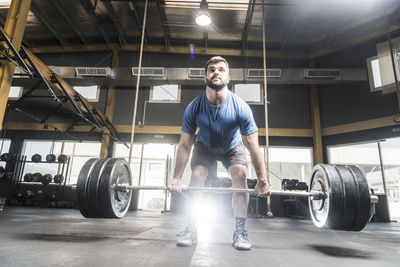 Young man lifting barbells at brightly lit gym