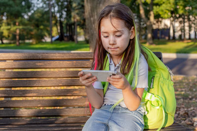 Young girl relaxing on park bench engaged with smartphone outdoors