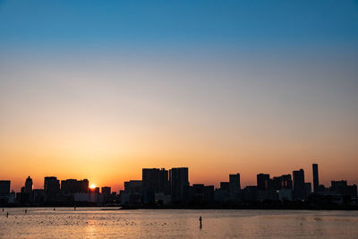 Silhouette buildings by sea against sky during sunset