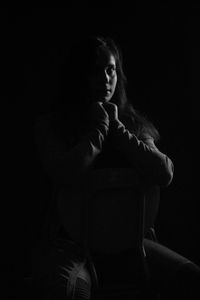 Thoughtful teenage girl sitting on chair in darkroom