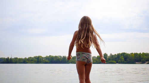 Shirtless girl walking at lakeshore against sky