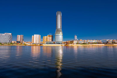 Buildings by river against clear blue sky