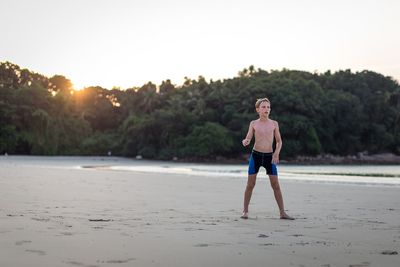 Full length of man standing on beach against sky during sunset