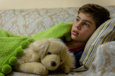 Boy with stuffed toy looking away while relaxing on sofa at home