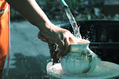 Cropped hands of person cleaning utensils with water