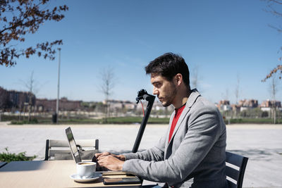 Side view of young man using mobile phone while sitting on table