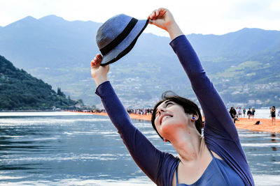 Young woman holding hat against mountains