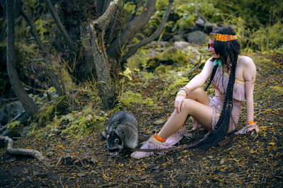 Woman with raccoon sitting in forest