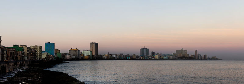 Sea by buildings against sky during sunset
