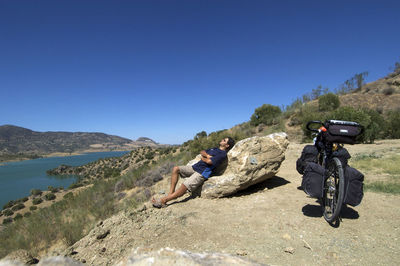 Men sitting on rock against clear blue sky