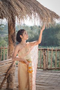 Girl in traditional clothing standing by thatched roof