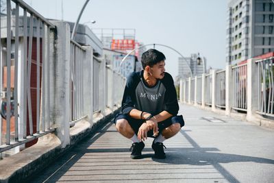 Young man sitting on wall in city against sky