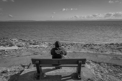 Rear view of woman sitting on beach against sky