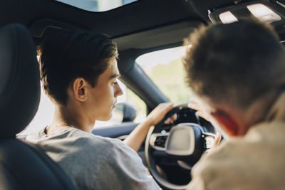 Father giving driving lessons to son while sitting in car