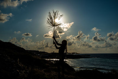 Silhouette person standing by sea against sky